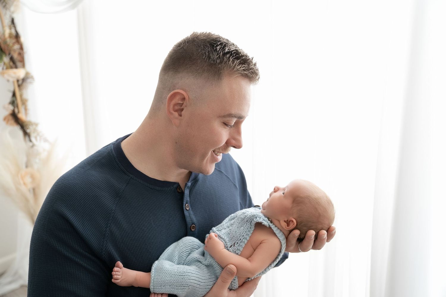 In central Minnesota a parent lovingly kisses newborn baby while holding them near a bright window during lifestyle photography session.