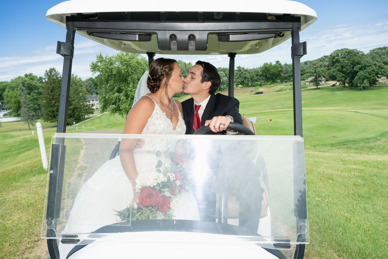 Bride and groom sharing a romantic kiss in a golf cart on a sunny green course.