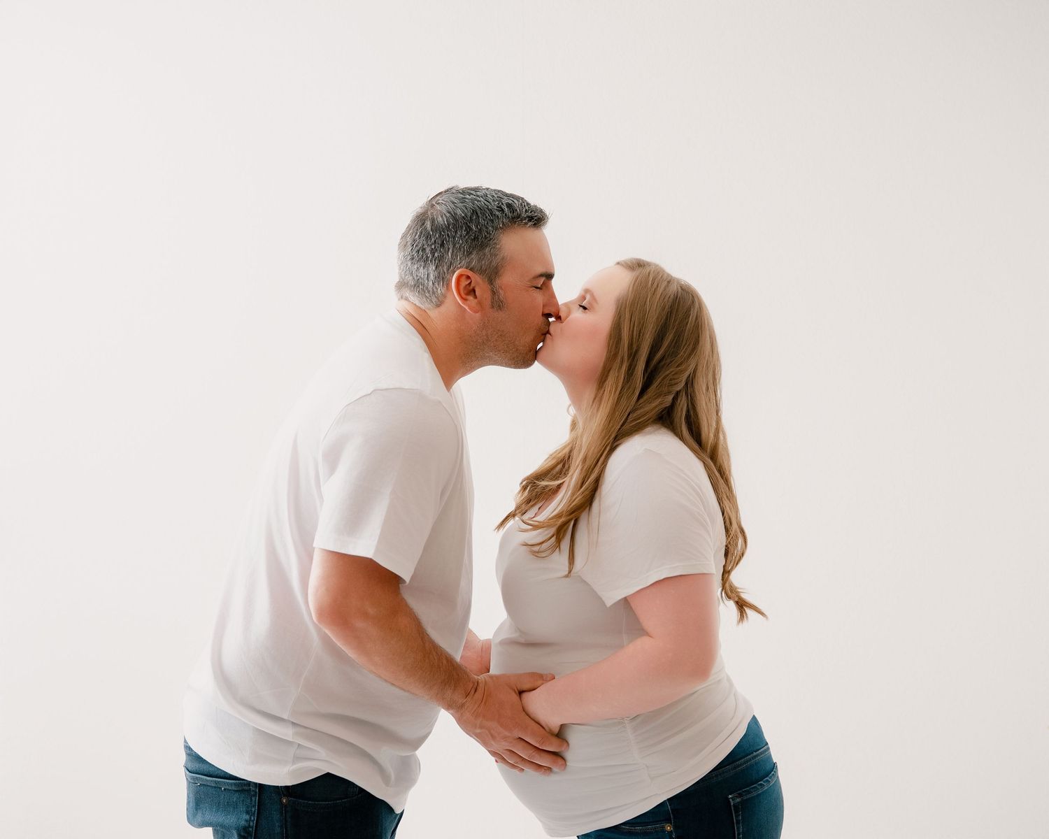 A couple wearing matching white shirts share an intimate kiss against a plain white background.