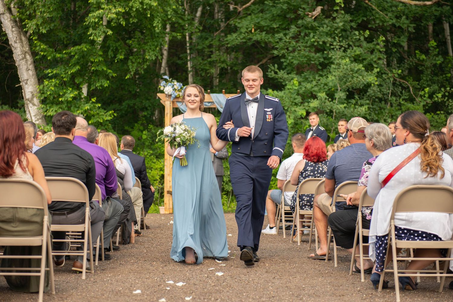 Wedding party members in blue and navy attire walk down the outdoor ceremony aisle. Zimmerman MN Weddings