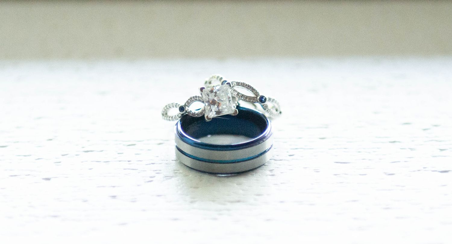 Diamond engagement ring and wedding bands arranged on blue and white striped surface. Zimmerman MN Weddings