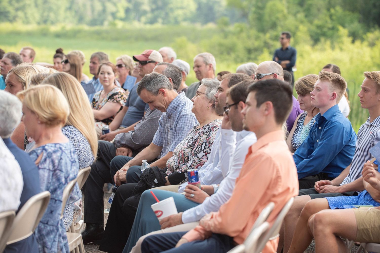Wedding guests seated in white chairs at an outdoor ceremony with lush greenery in the background. Zimmerman MN Weddings