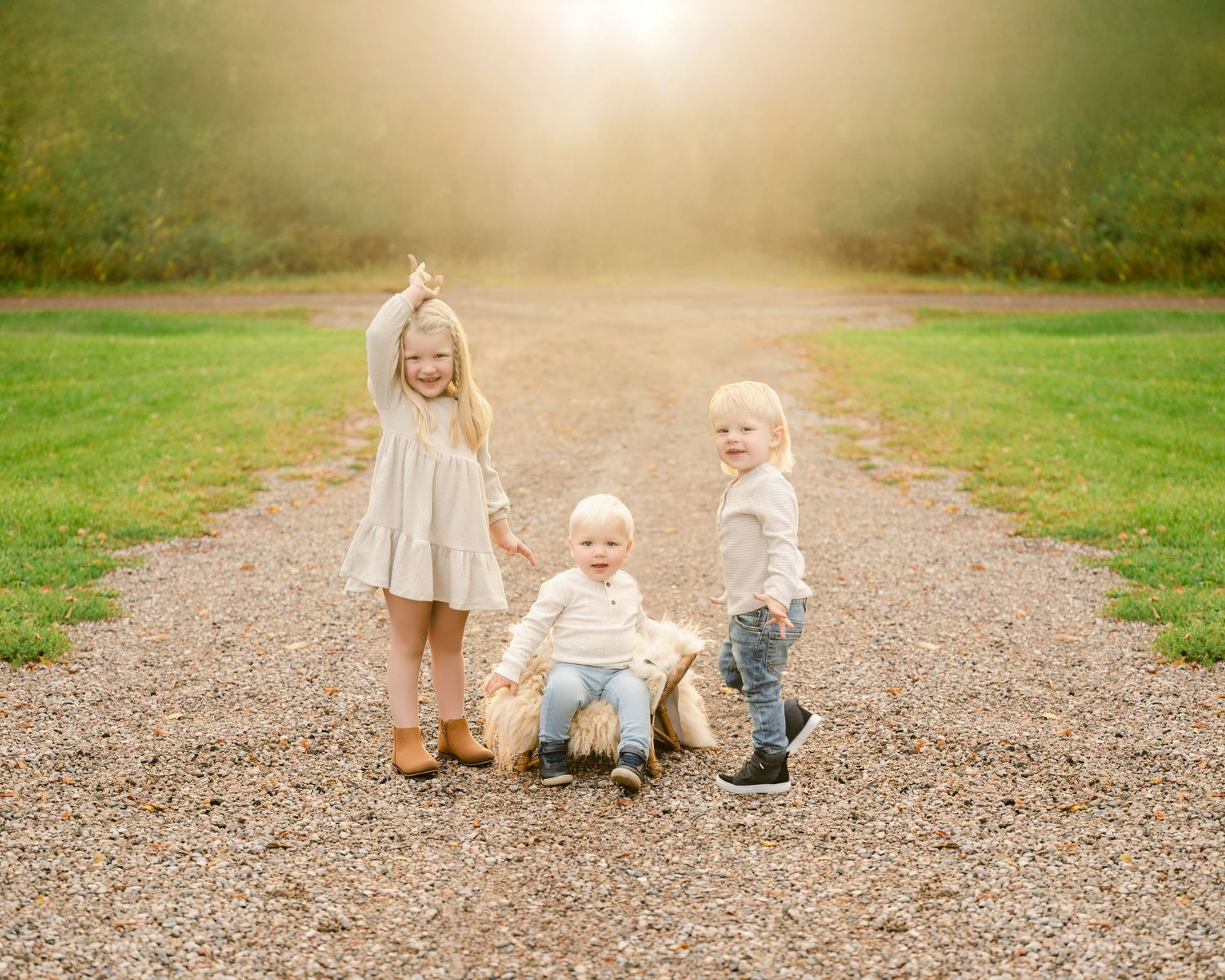 Three small children play together on a gravel path surrounded by green grass on a misty morning.
