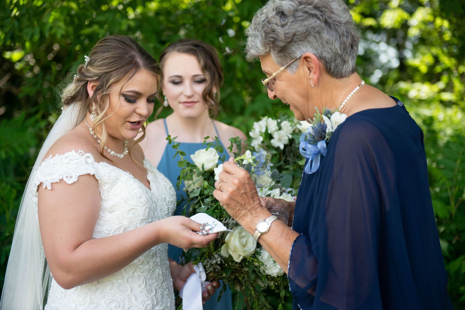 Three women share a special moment with flowers during wedding preparations. Zimmerman MN Weddings