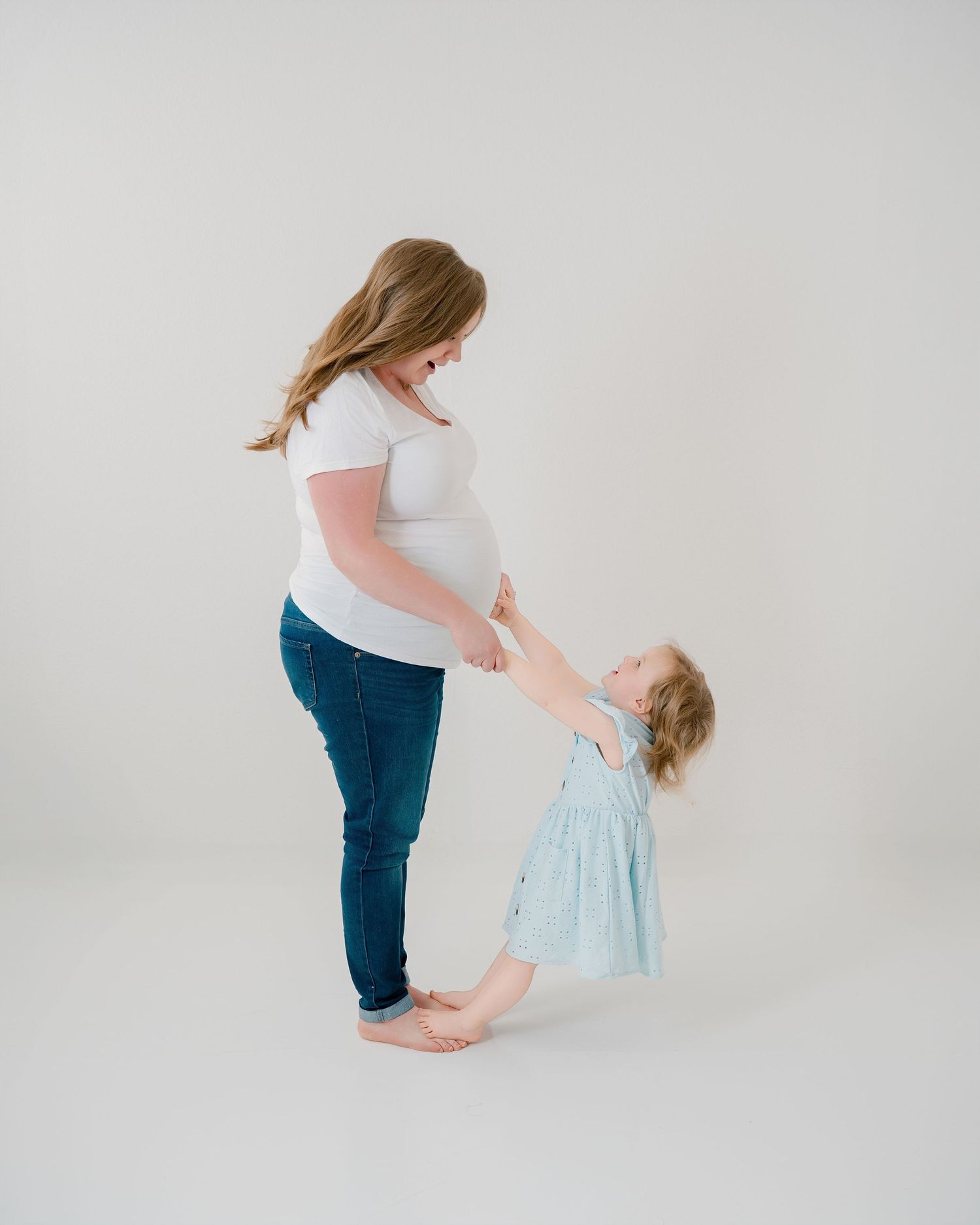 A person in blue jeans interacts with a baby in a soft mint green outfit against a white background.