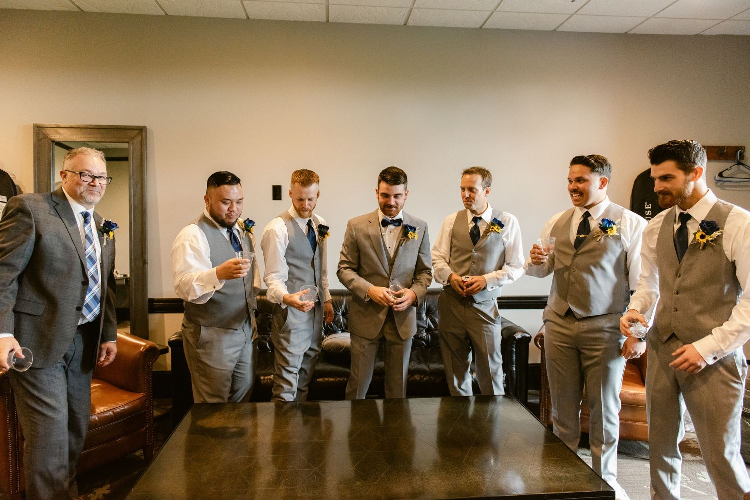 Central MN Wedding Photos | Groom and groomsmen laughing together in grey suits and bow ties during wedding day preparations.