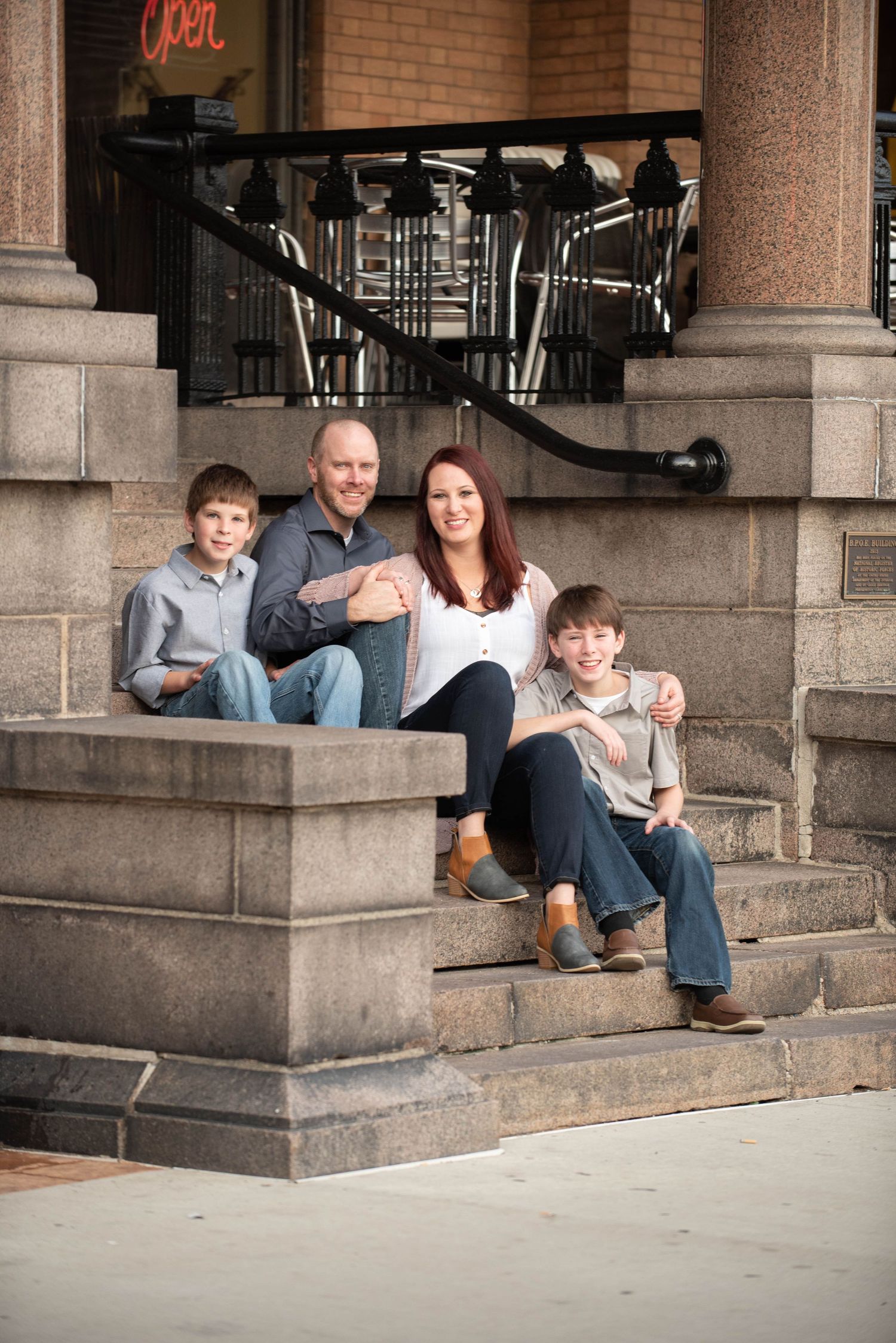 Family sitting together on stone steps outside a brick building with classic architecture.