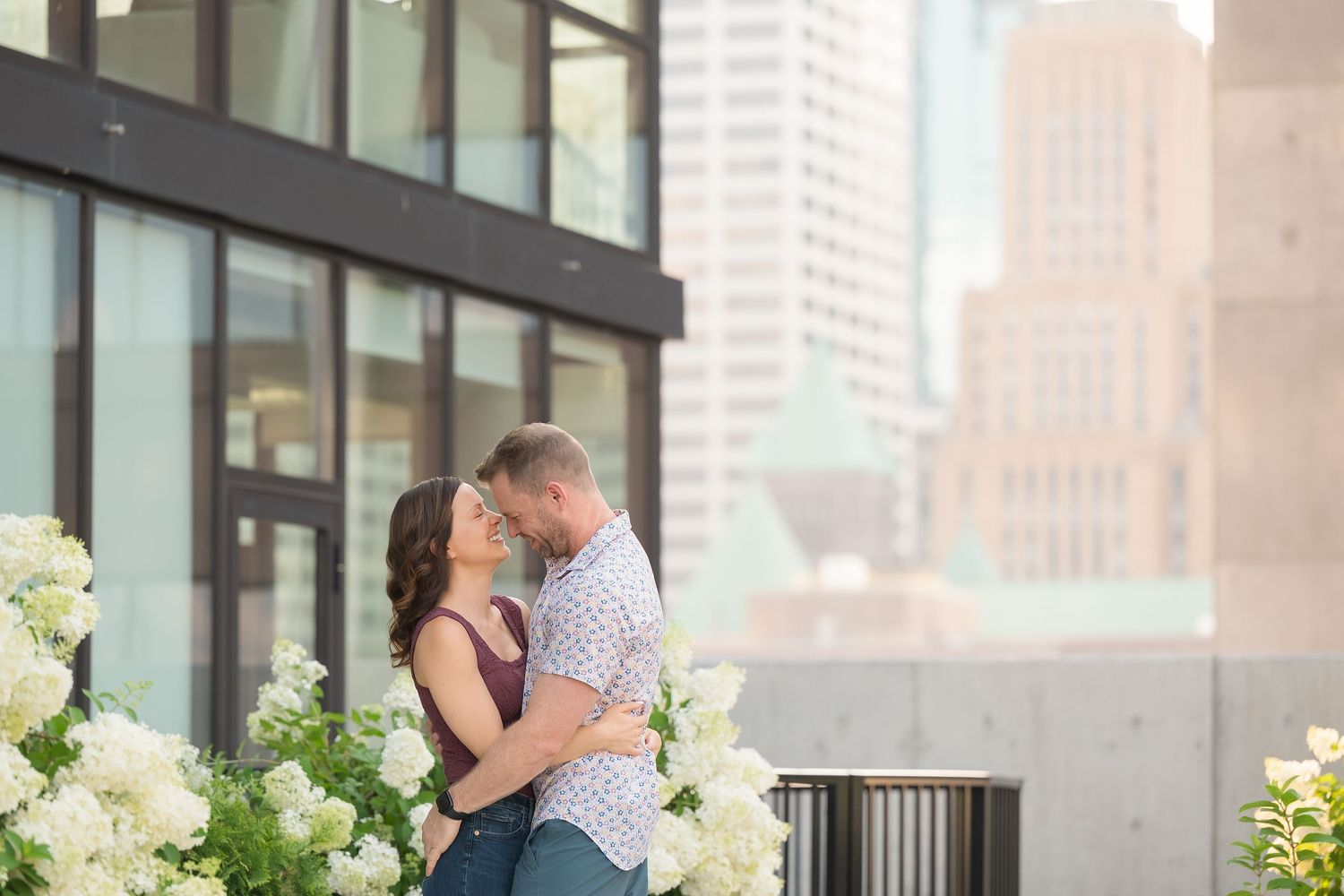 A couple shares a romantic moment on a city rooftop terrace with white floral arrangements and urban buildings in background.