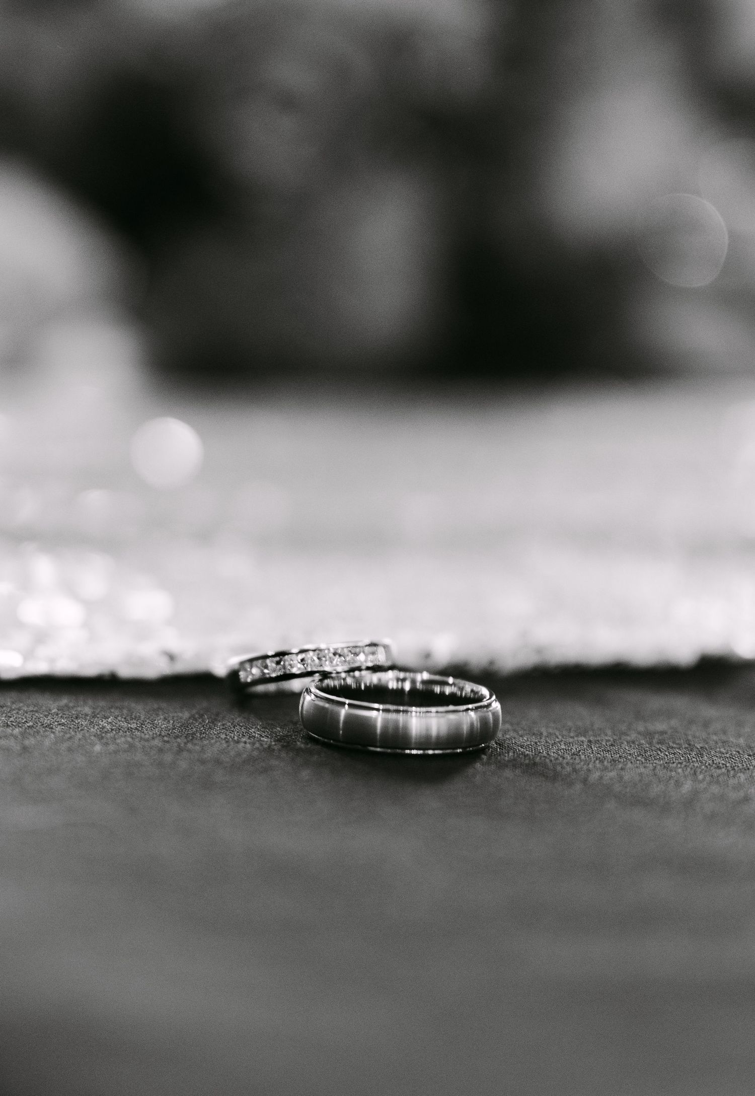 Black and white close-up of two wedding rings on a textured surface with soft bokeh background.