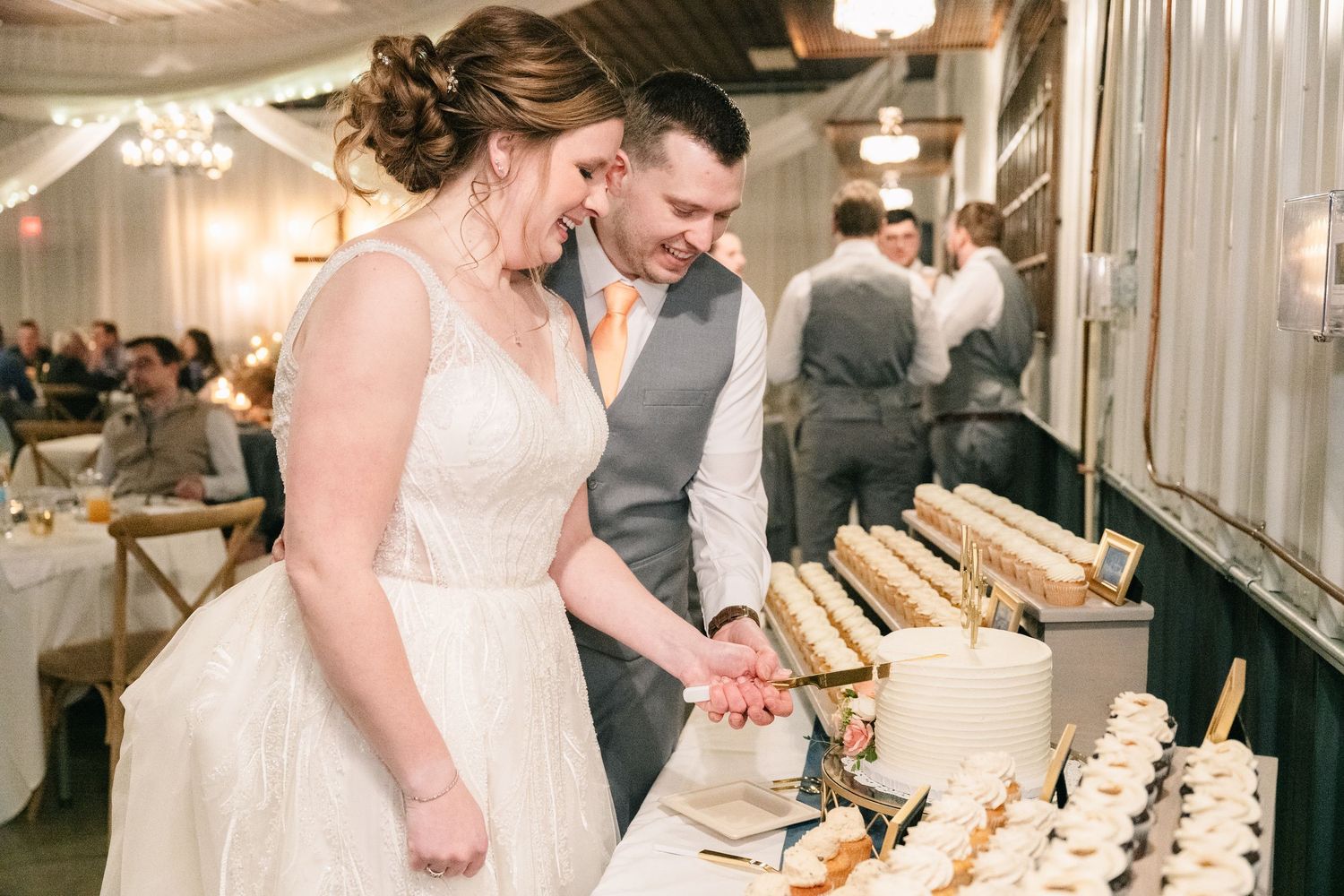 Bride and groom smiling while cutting their wedding cake at a elegant reception venue.