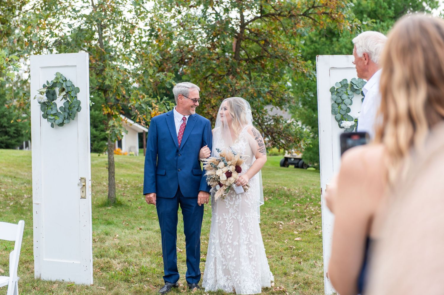Outdoor wedding ceremony setup with vintage white doors creating unique entrance walkway.