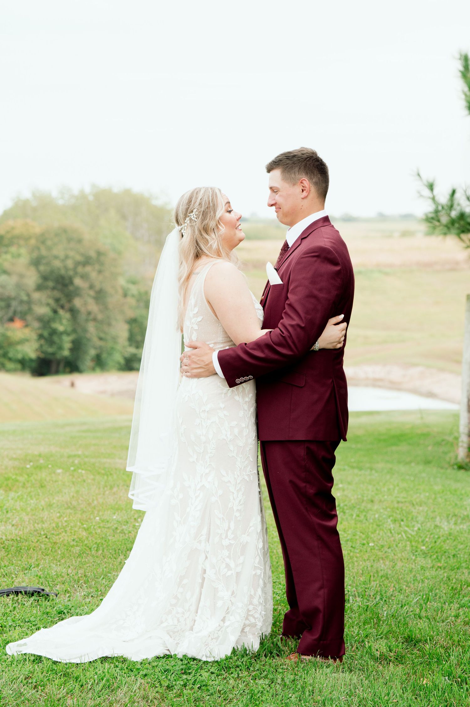 Couple shares an intimate moment in their wedding attire on a grassy hill during an outdoor ceremony.