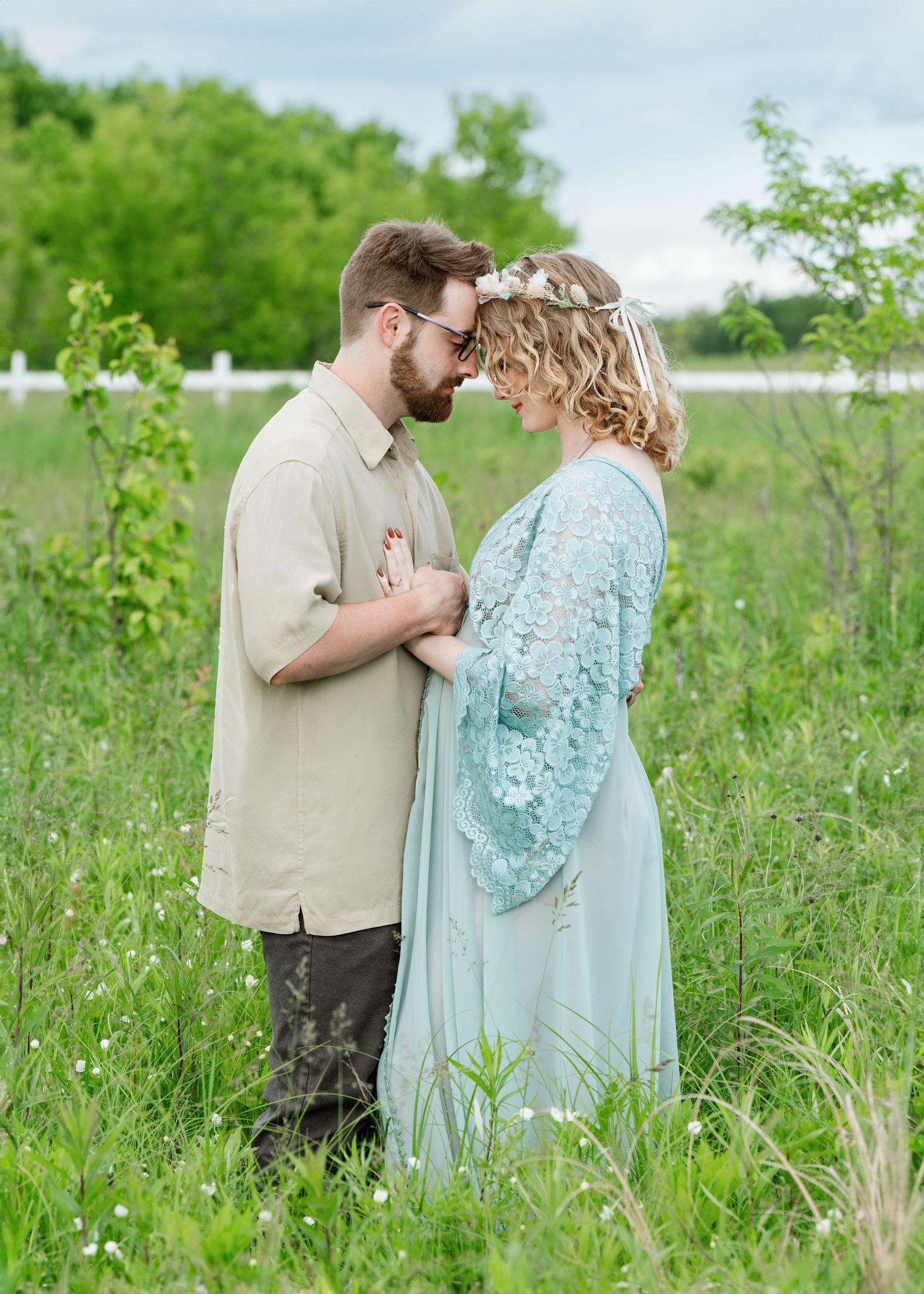 A couple embraces in a romantic moment among wildflowers and tall grass on a spring day wearing mint green and beige. Princeton MN Milestone