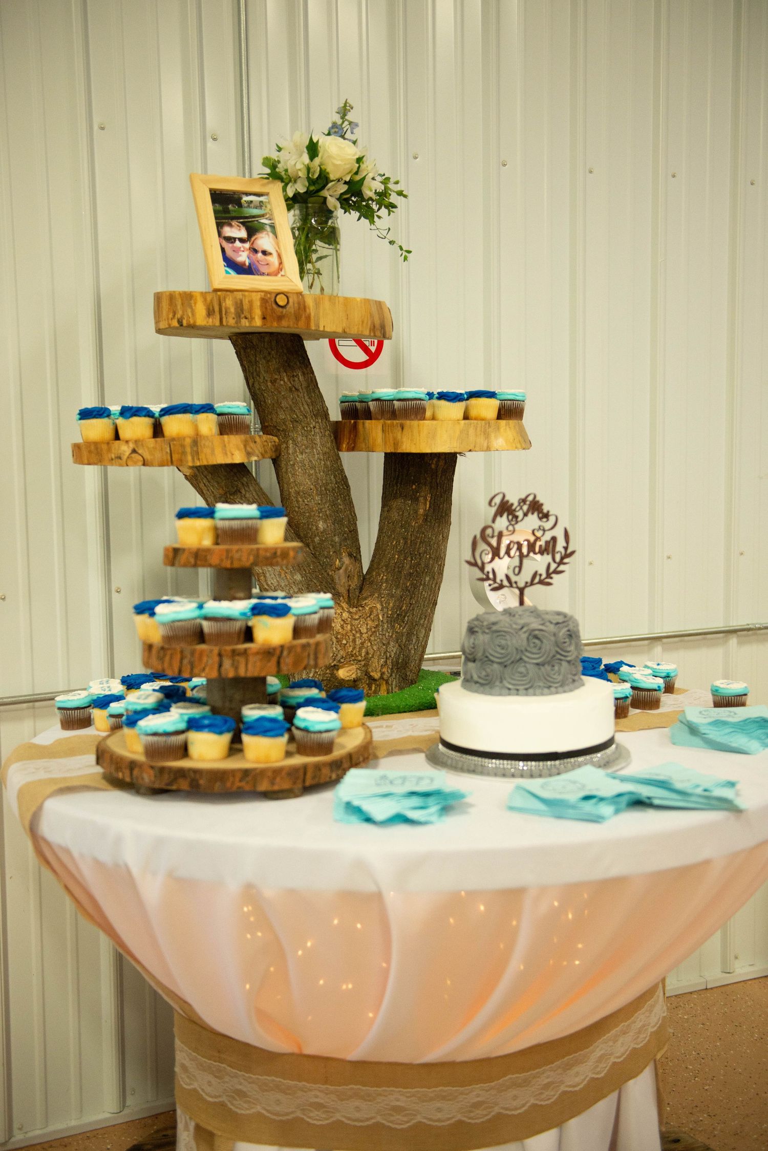 Elegant wedding dessert table with wooden tree trunk stands holding cupcakes and a decorated cake with teal accents. Zimmerman MN Weddings