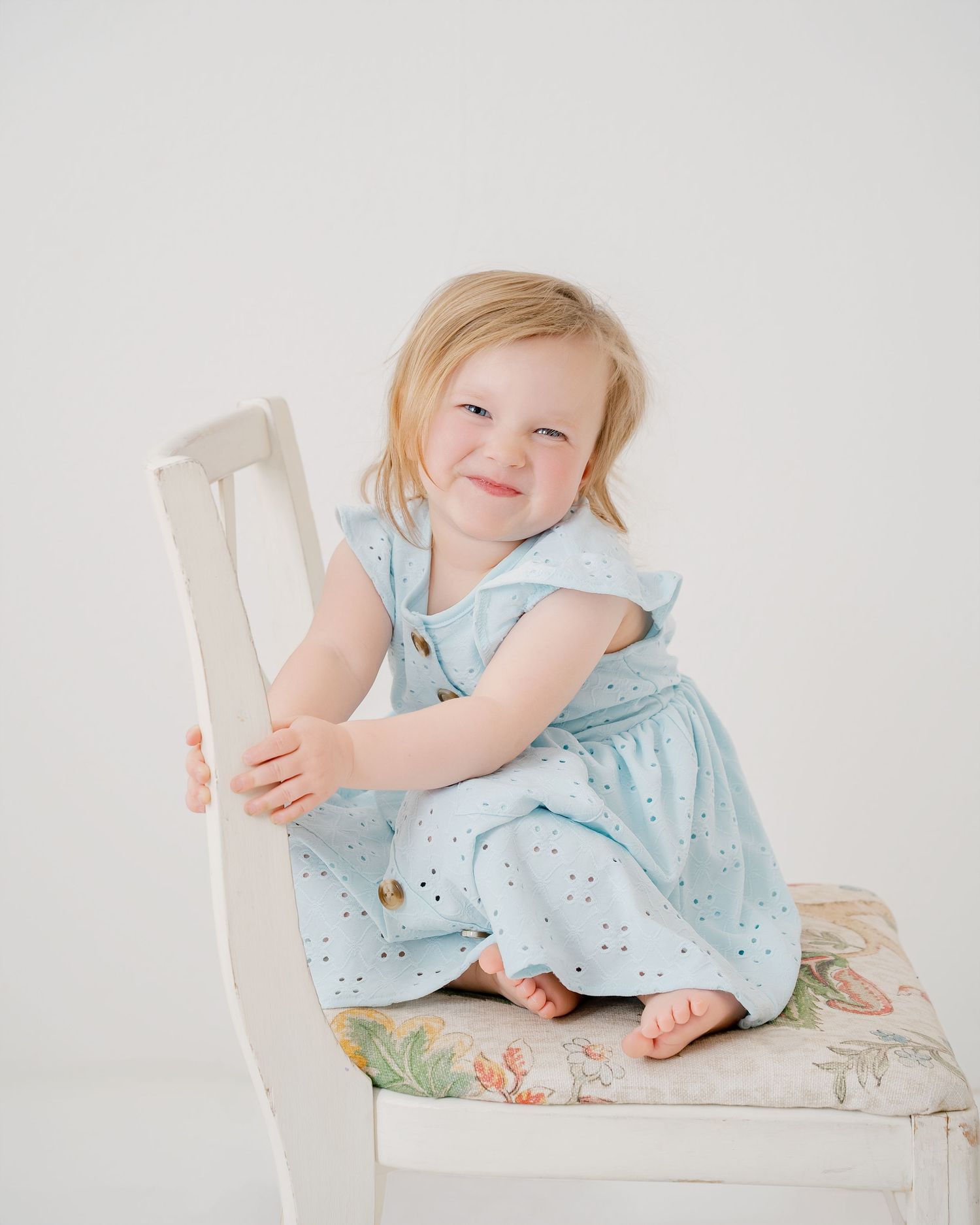 Child in light blue dress sitting on white chair showing candid expressions in series of photos.