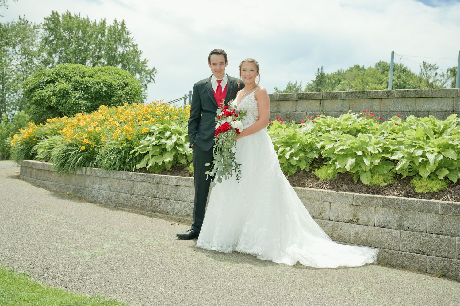 Bride and groom pose together on a garden path with vibrant yellow flowers in the background.