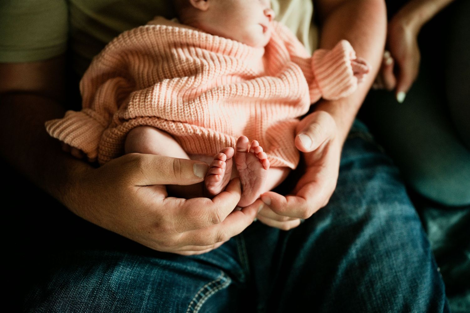 Parents cradling a newborn baby in pink knit outfit, close-up of tiny feet in loving hands.
