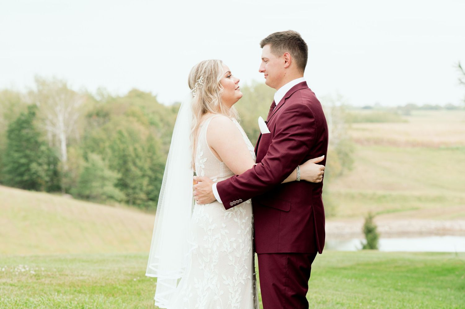 A romantic outdoor wedding portrait featuring a couple embracing, with the bride in white and groom in burgundy.