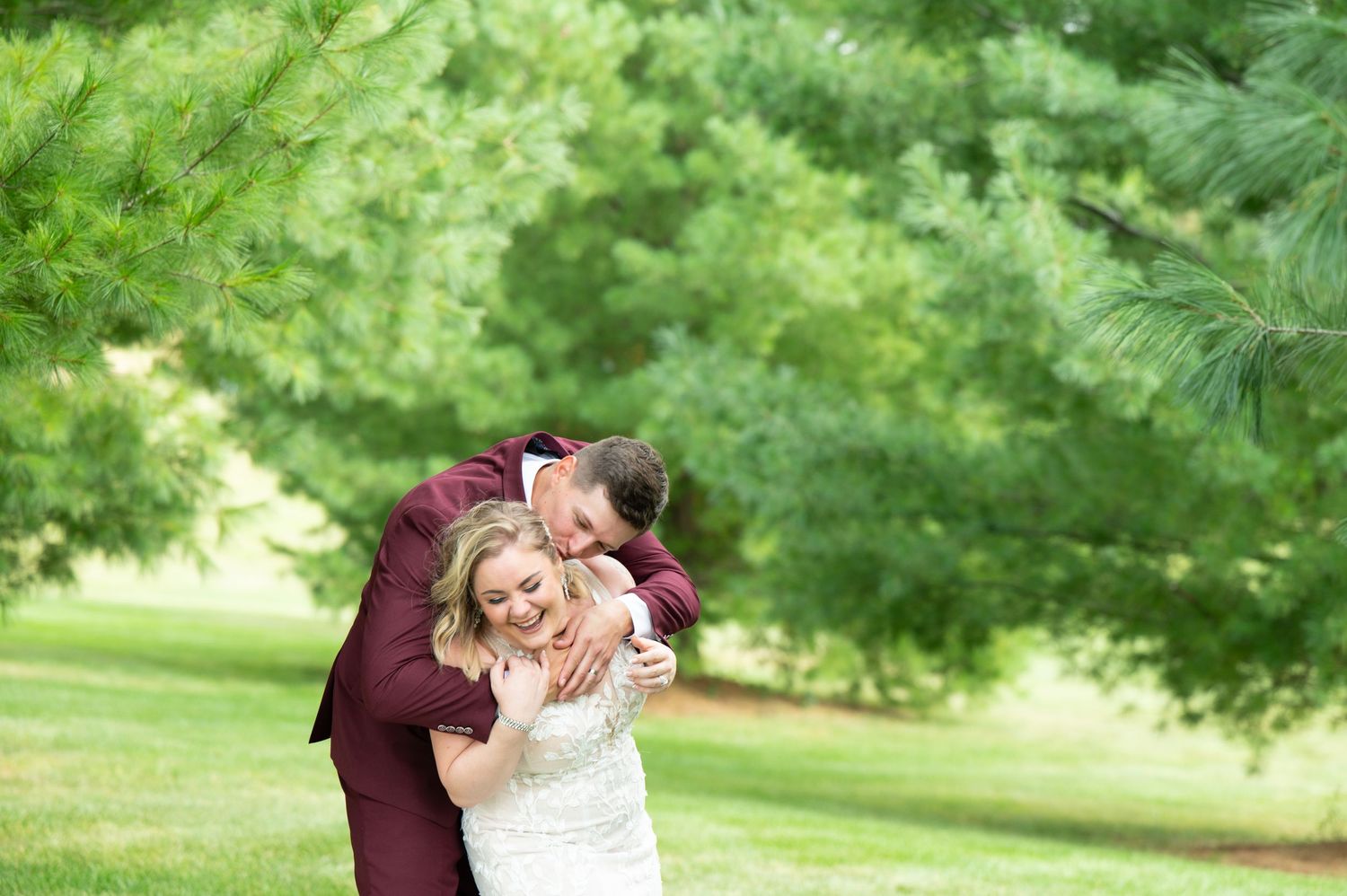 Candid wedding moments captured in lush green garden setting with burgundy and white attire.