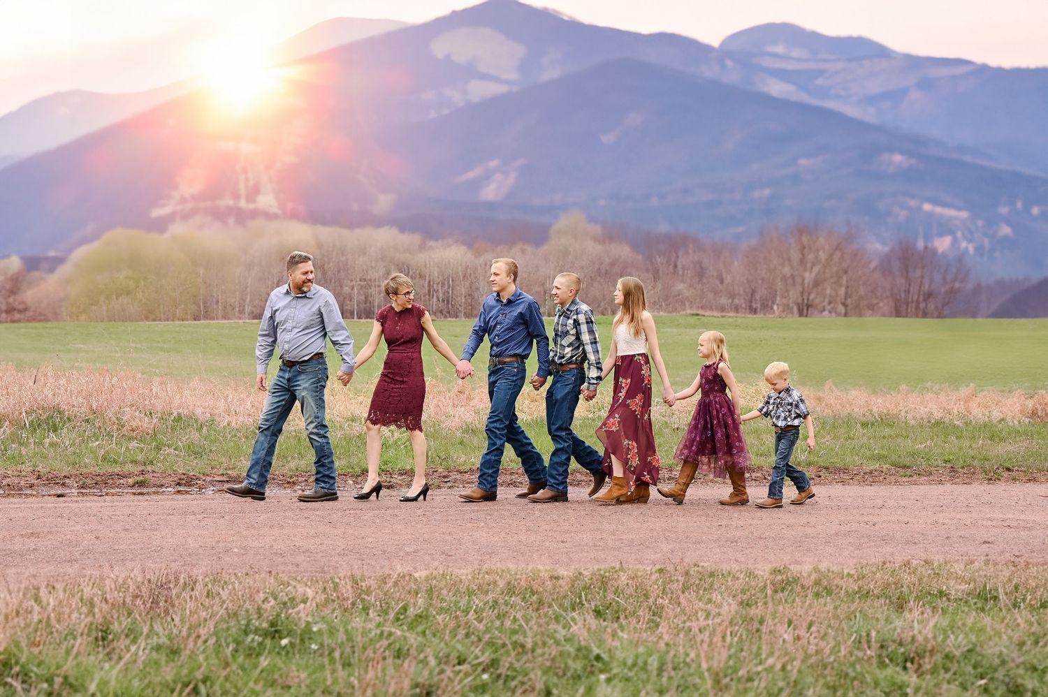 A group walks together on a dirt path at sunset with mountains in the background and sun flare lighting the scene.
