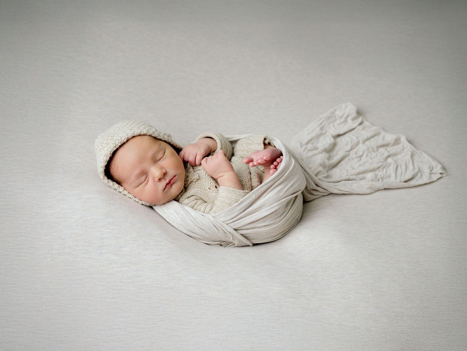 Minnesota Best newborn photographer - Peaceful newborn baby wrapped in soft white fabric lies sleeping on a neutral grey background.