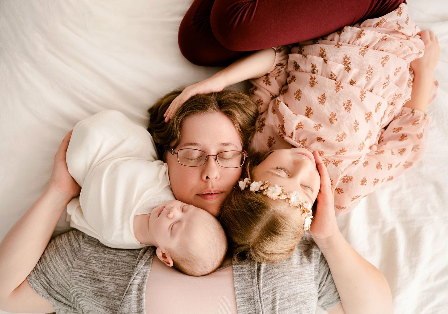 Three people lying peacefully together on white bedding, wearing comfortable casual clothing.
