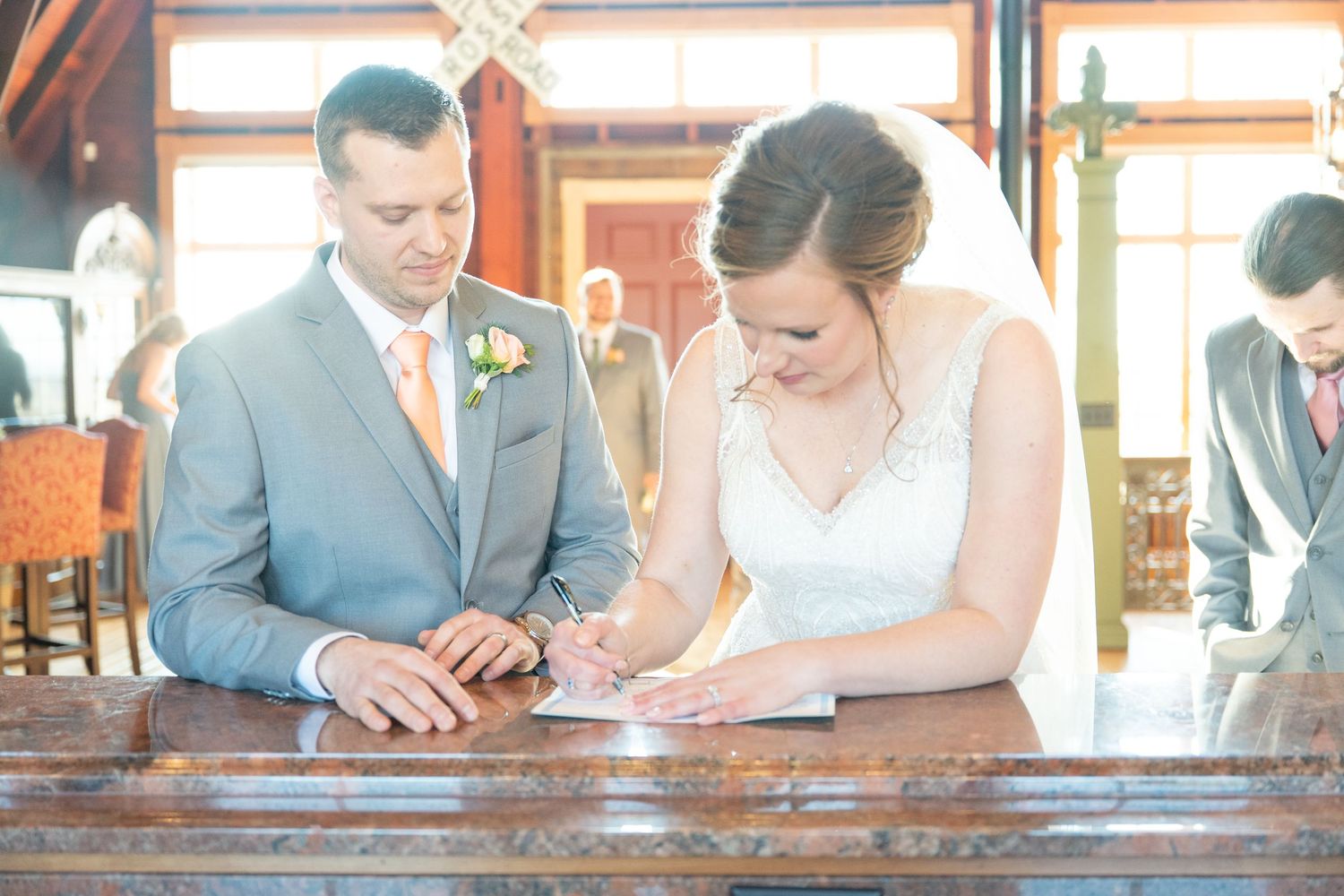 Bride and groom signing their wedding certificate together at a wooden table during the ceremony.