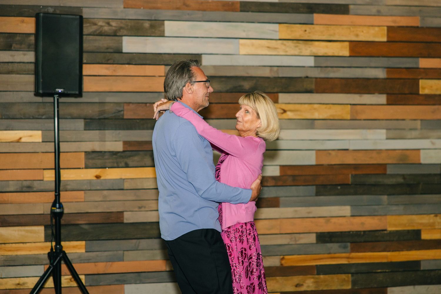 Older couple shares a romantic dance in front of a colorful reclaimed wood wall.