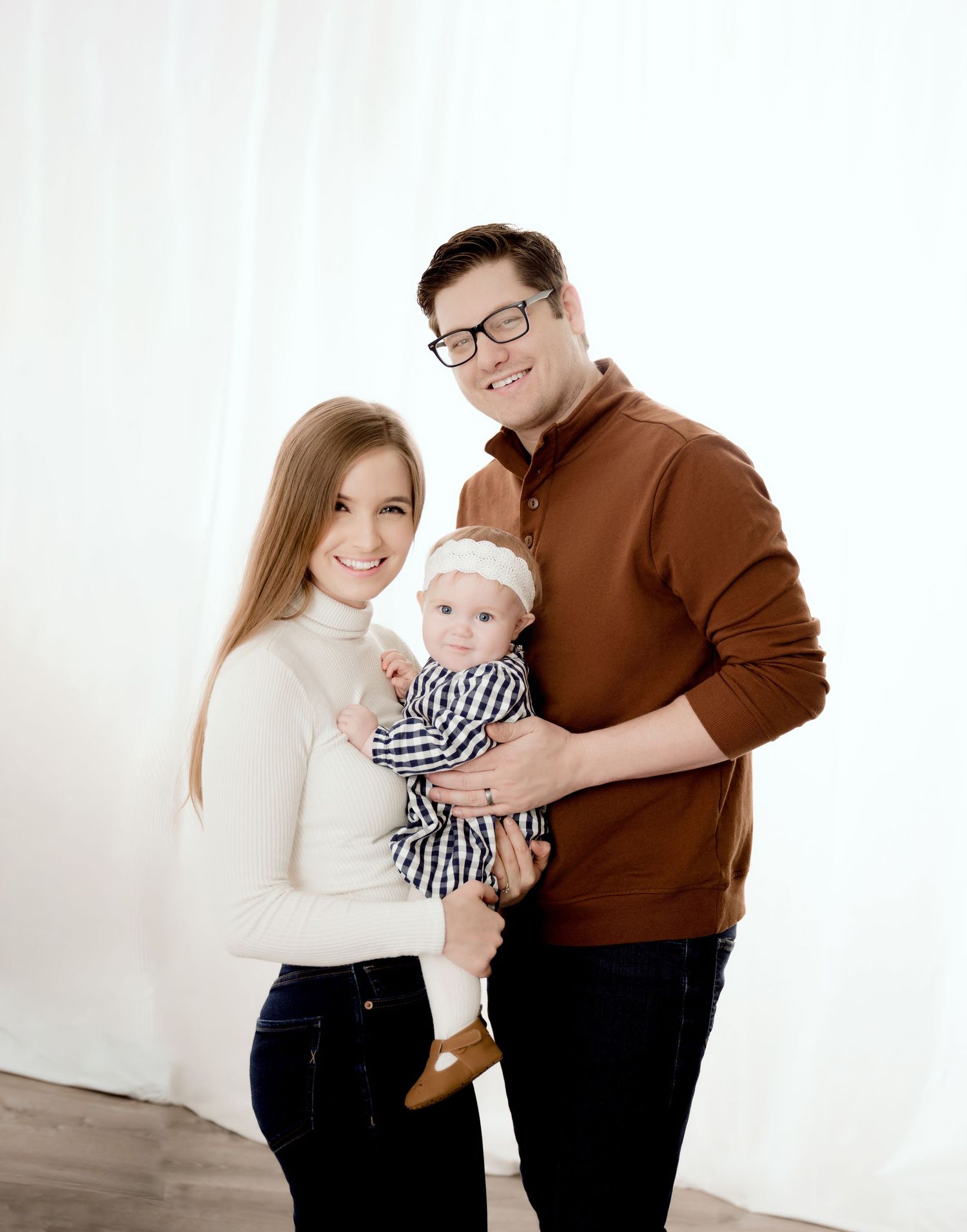 Professional studio portrait of family in coordinated brown and white outfits.