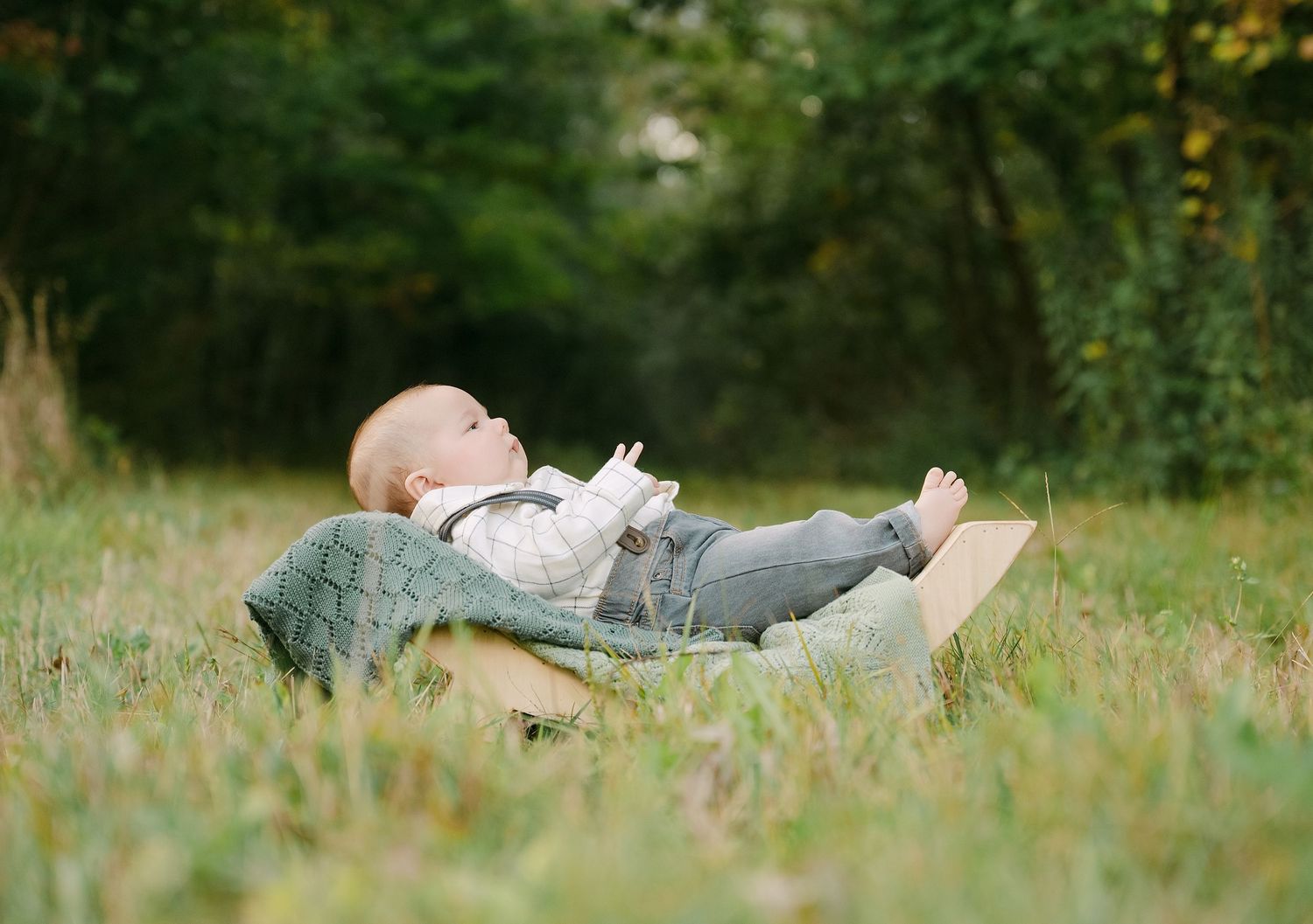 Baby lying on grass outdoors wearing white shirt and gray pants in natural setting.. Minnesota milestone photographer