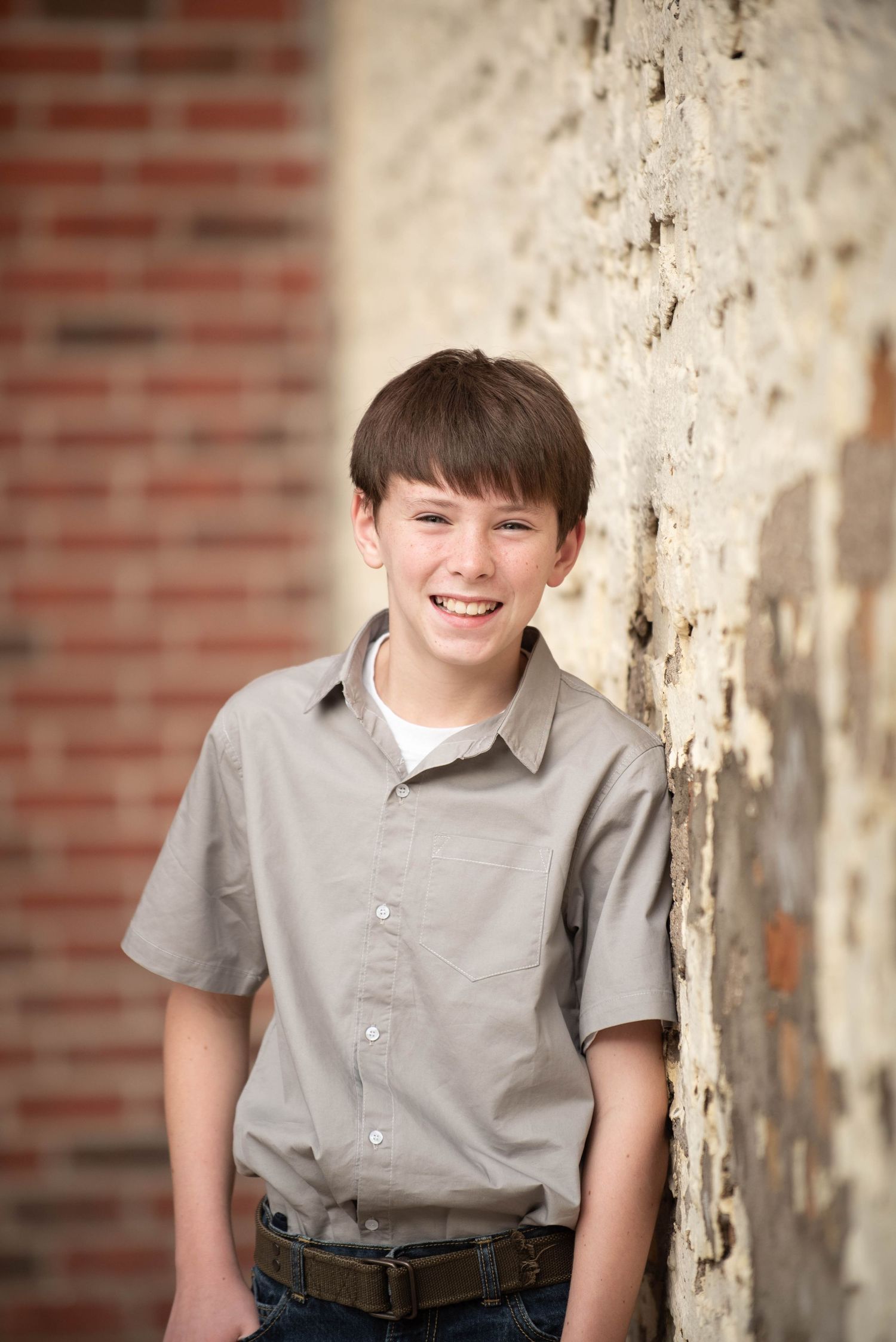 Candid portrait of a young student in a grey uniform shirt against a textured wall background.