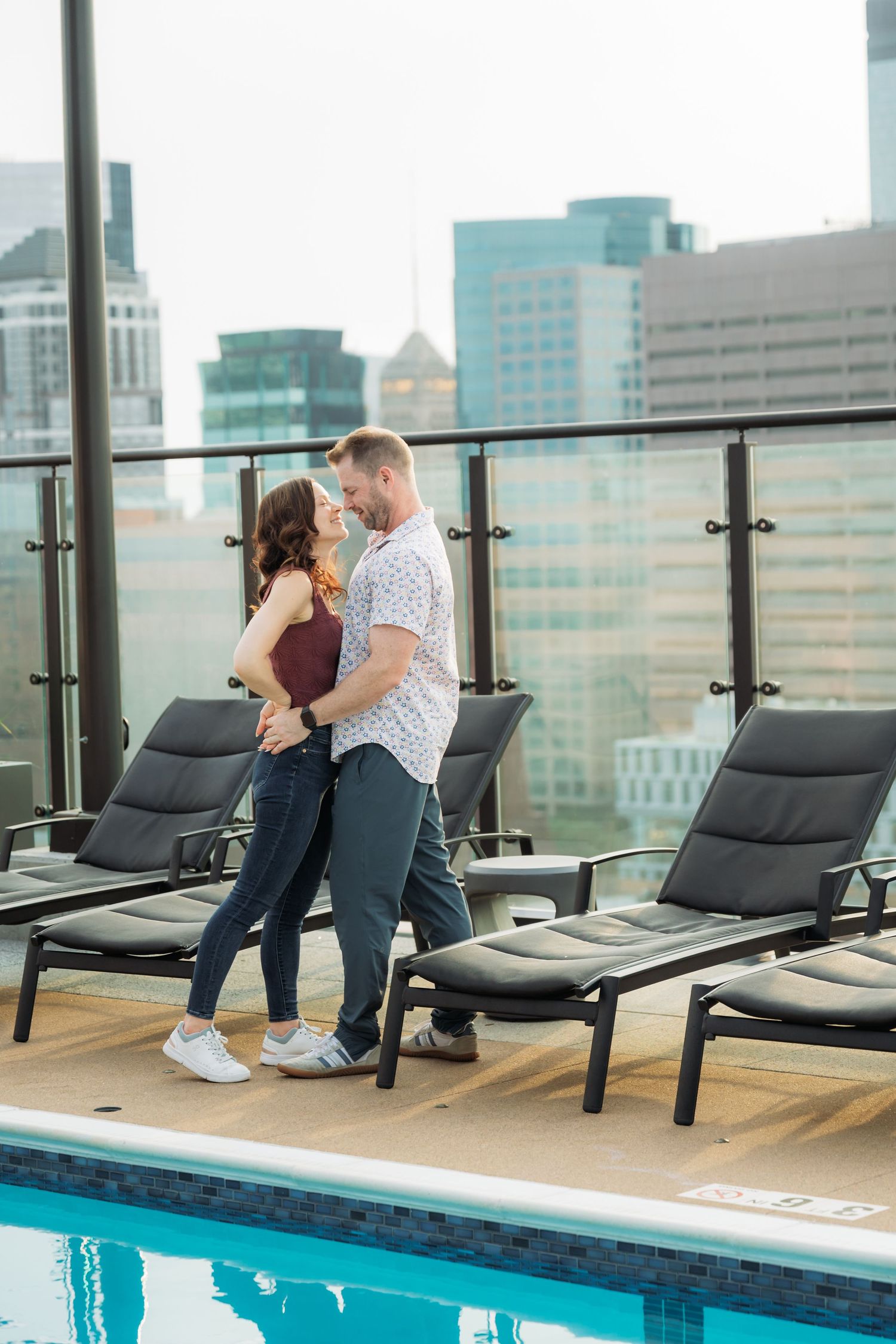 A couple shares an intimate moment by an indoor rooftop pool with city skyline views.