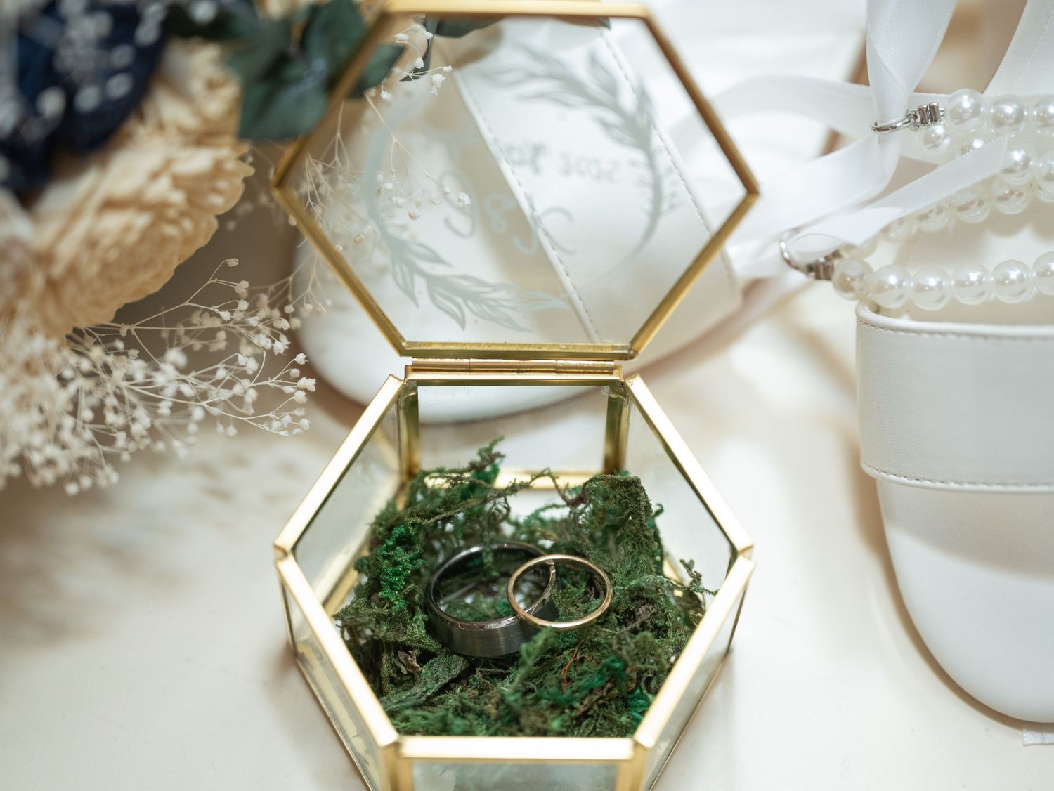 Wedding rings nestled in a hexagonal glass display box filled with green moss at Northern Lights near Milaca MN..