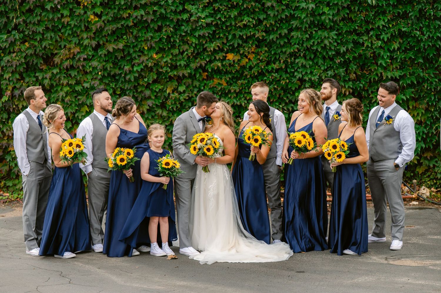 Central MN Wedding Photos | Bride and groom kissing surrounded by wedding party with sunflower bouquets.