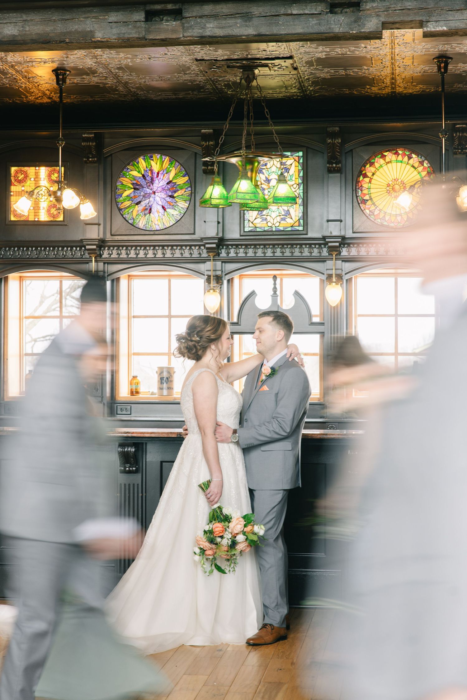 Bride and groom share an intimate moment surrounded by blurred wedding guests in a historic bar.