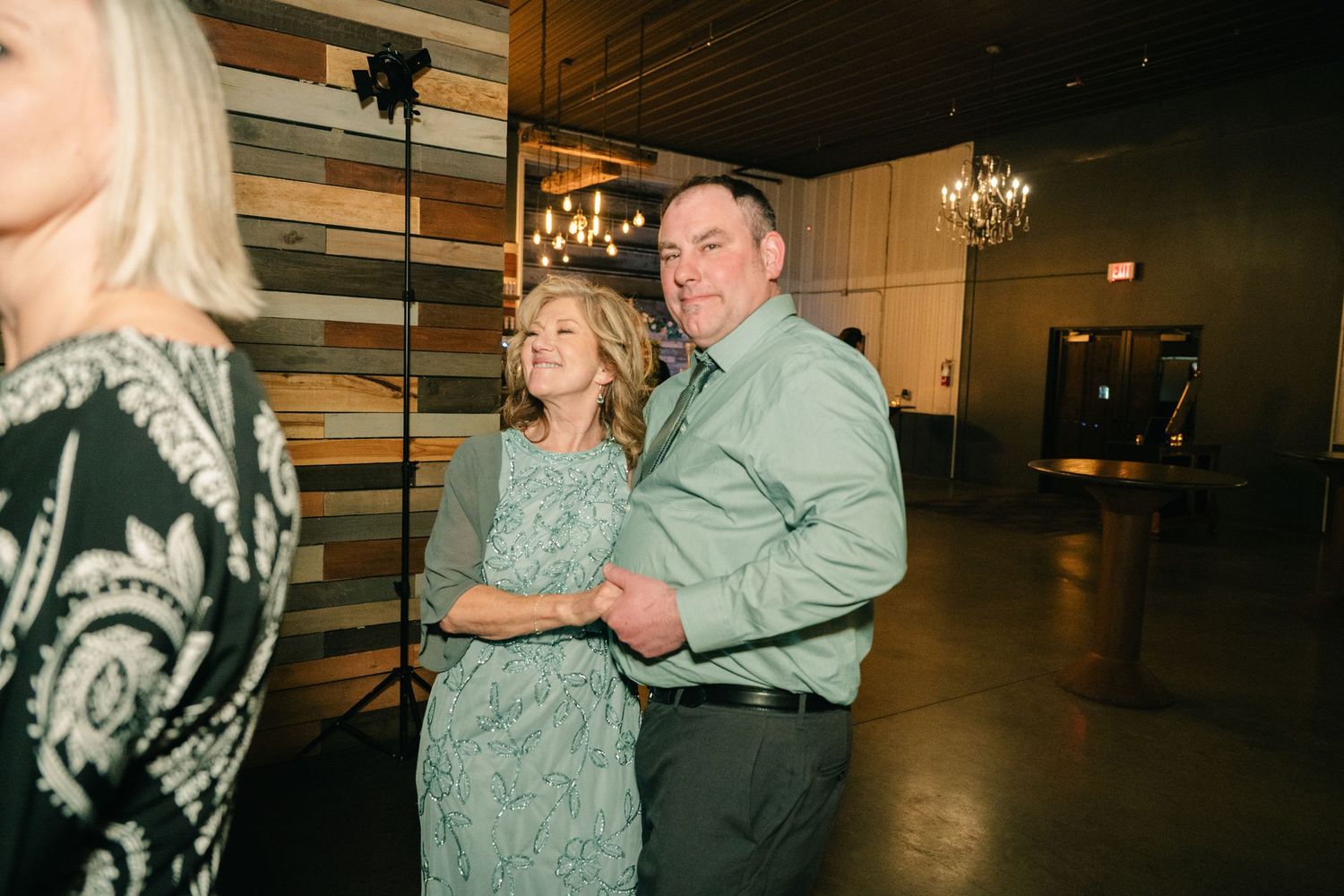 Couple in coordinating green outfits share a dance together at a wedding reception venue.