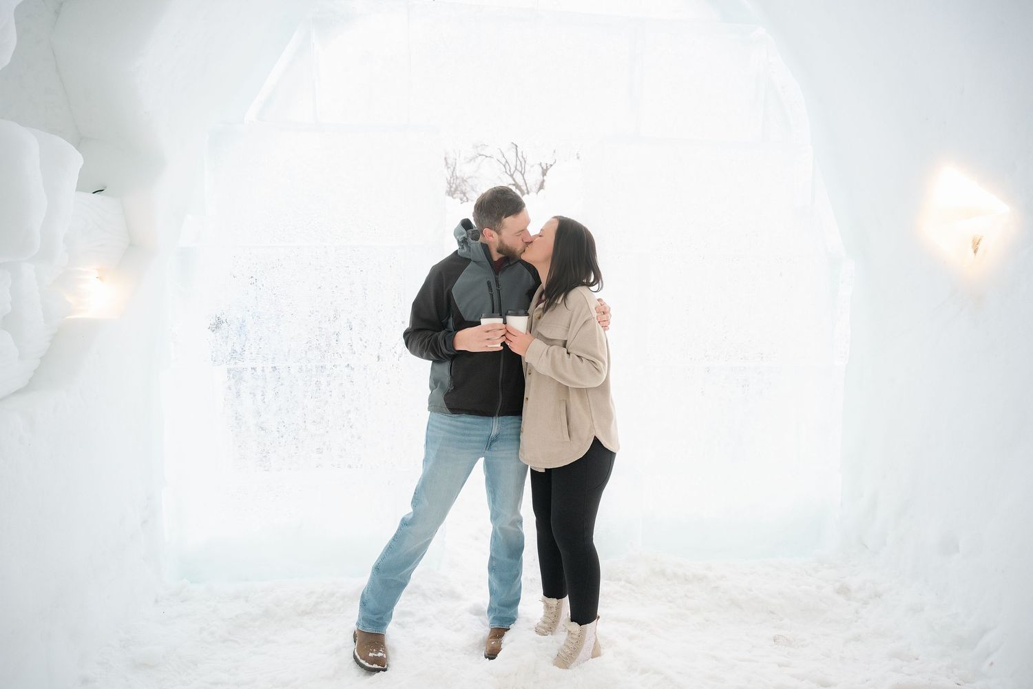 Couple sharing a romantic moment inside a snowy ice hotel, holding drinks and embracing warmly. Engagement Minneapolis MN