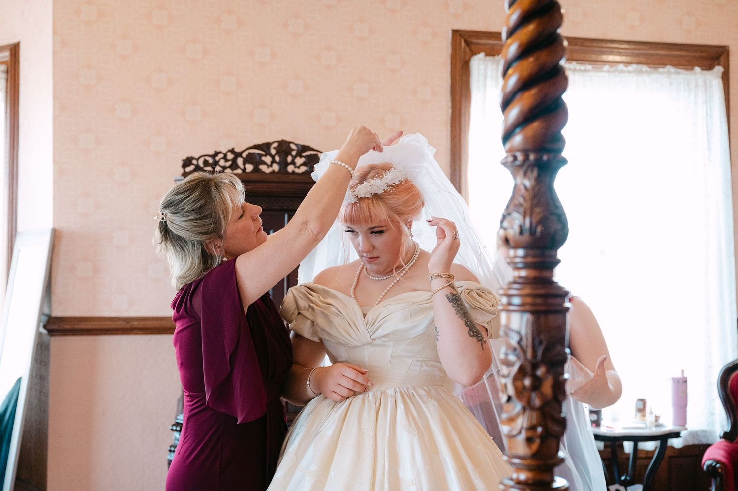 Central MN Wedding Photos | Woman in burgundy dress adjusting bride's veil and hair accessories before the wedding ceremony.