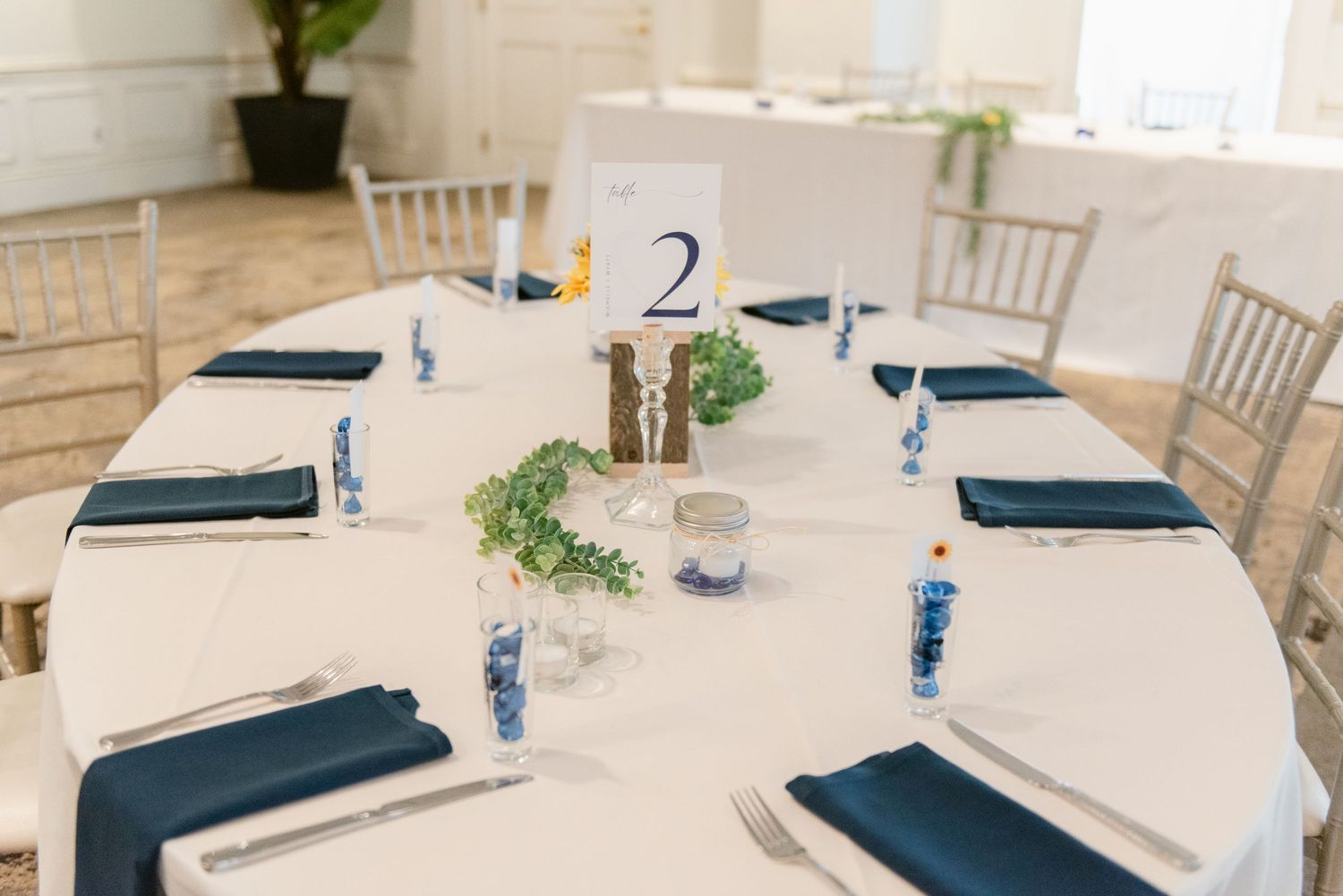 Central MN Wedding Photos | Elegant wedding reception table set with navy napkins, greenery centerpiece, and number two card.