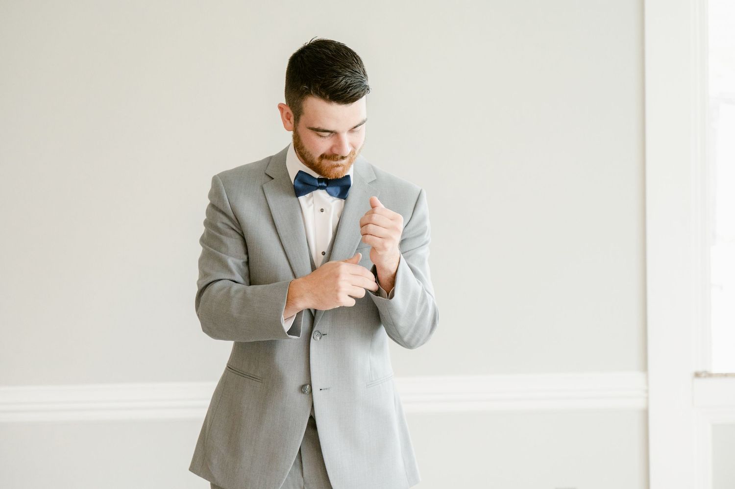 Central MN Wedding Photos | Dapper groom in gray suit and navy bow tie adjusts cufflinks while getting ready for wedding.