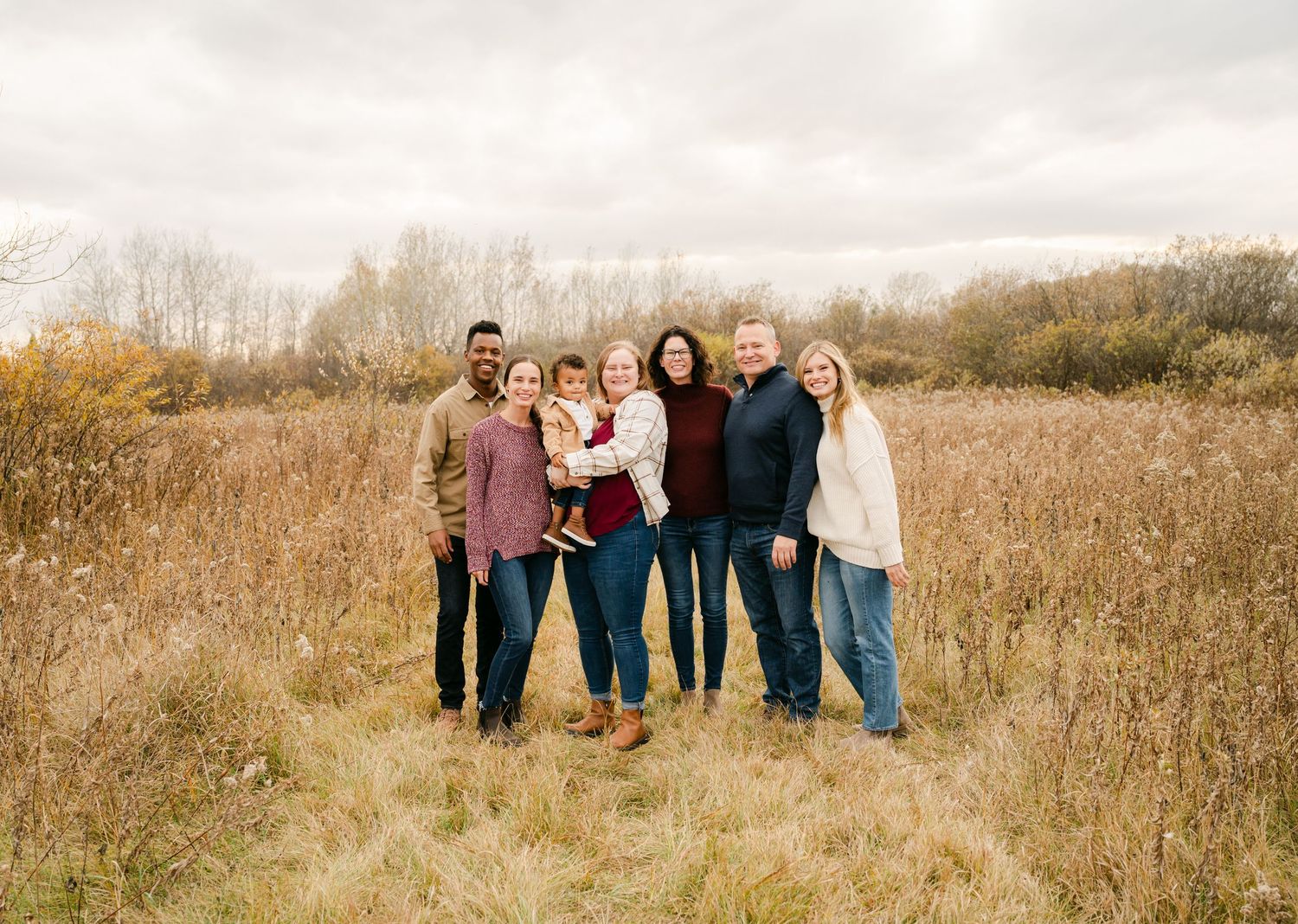 A group stands together in a golden autumn field on an overcast day with dried grasses and trees in the background.