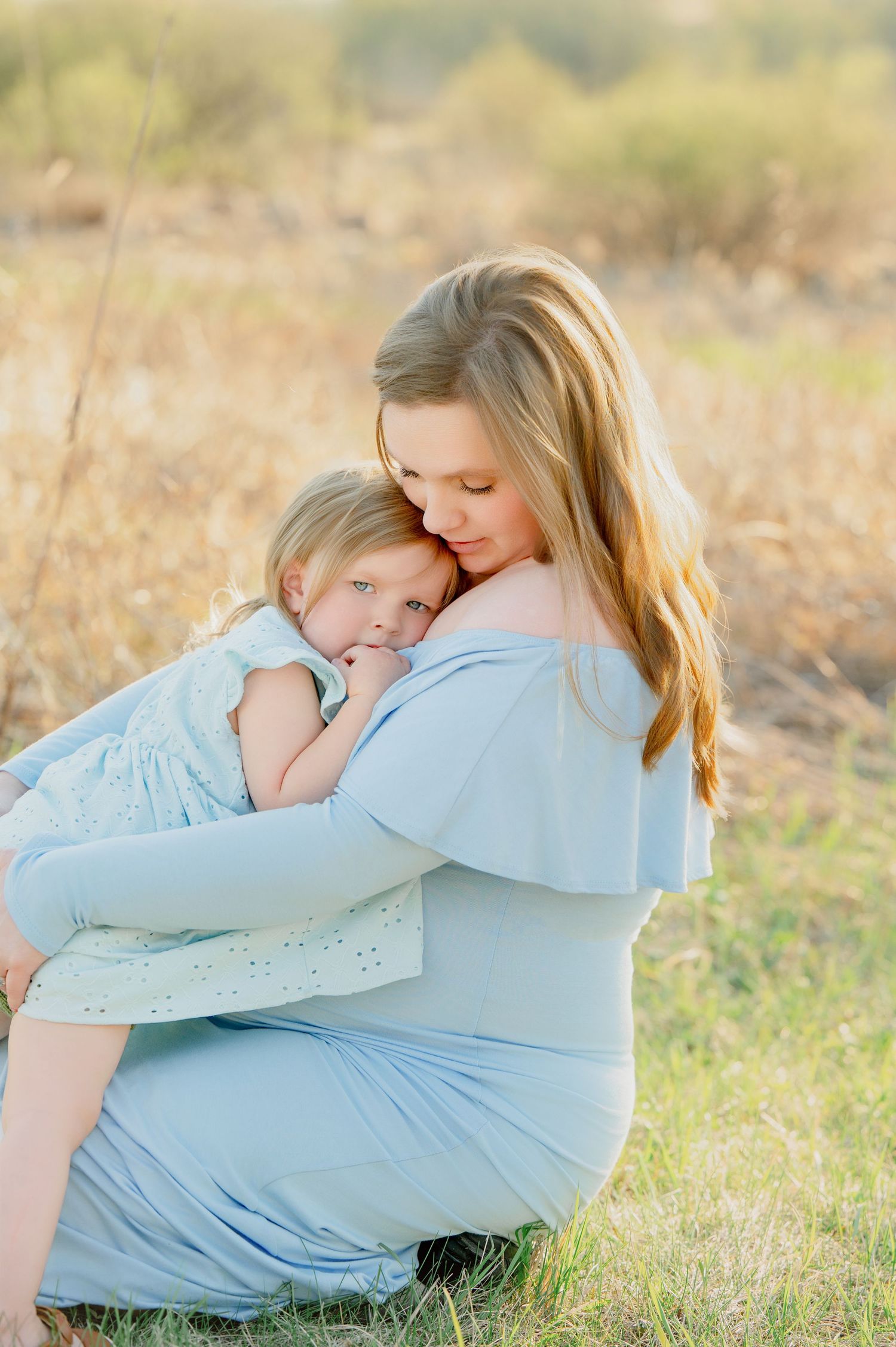 A tender family moment captured in soft sunlight as a child embraces a pregnant woman in a light blue dress.