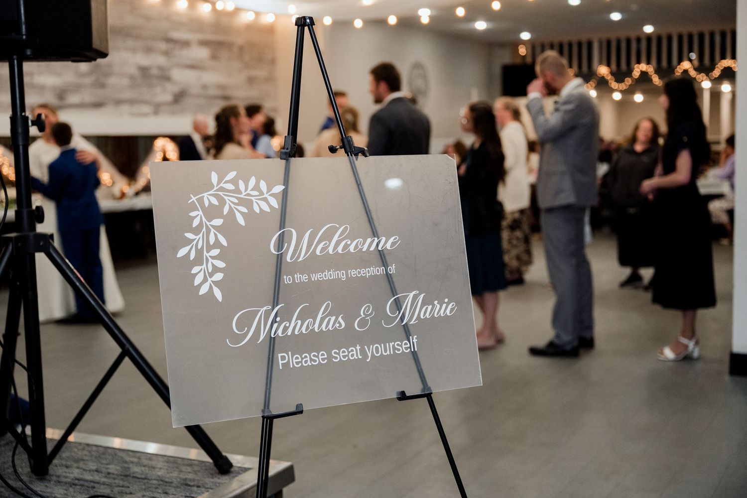 Elegant grey welcome sign with floral design displayed on easel at wedding reception entrance.