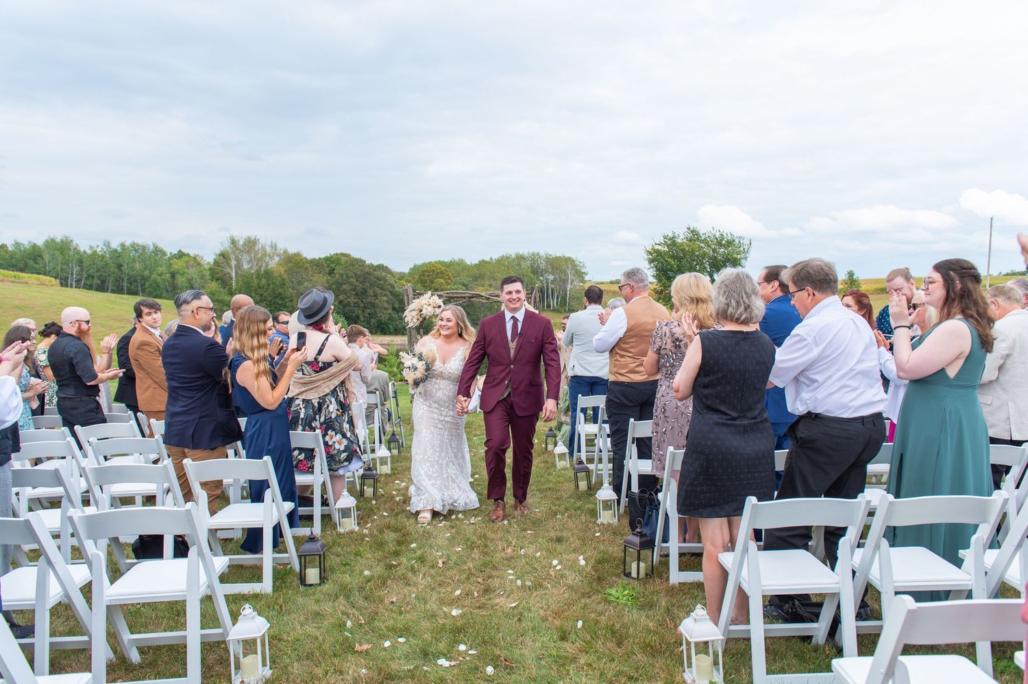 Wide angle view of wedding guests seated in rows of white chairs at an outdoor venue.