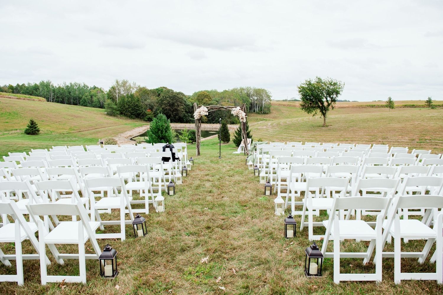 White ceremony chairs arranged on rolling hillside for outdoor wedding with scenic countryside views.