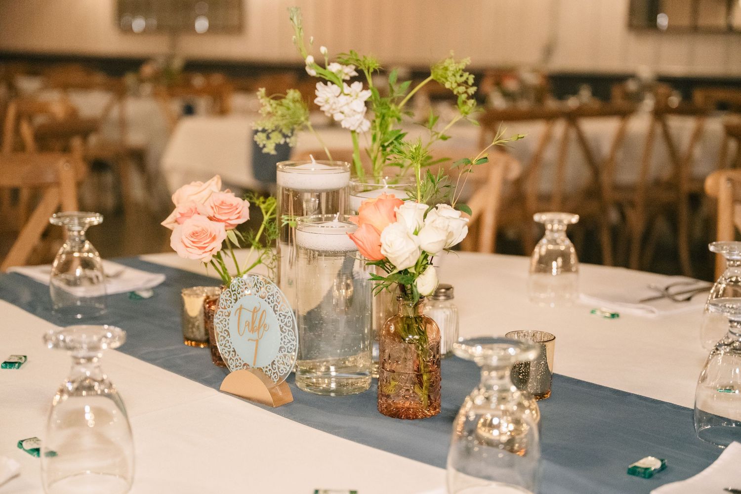 Elegant wedding reception table with pink roses, floating candles, and blue table runner centerpiece.