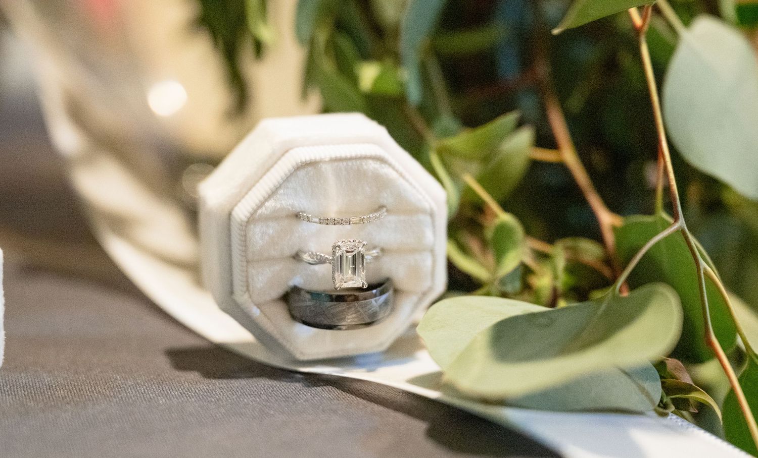 Wedding rings displayed in white octagonal velvet ring box surrounded by green eucalyptus leaves.