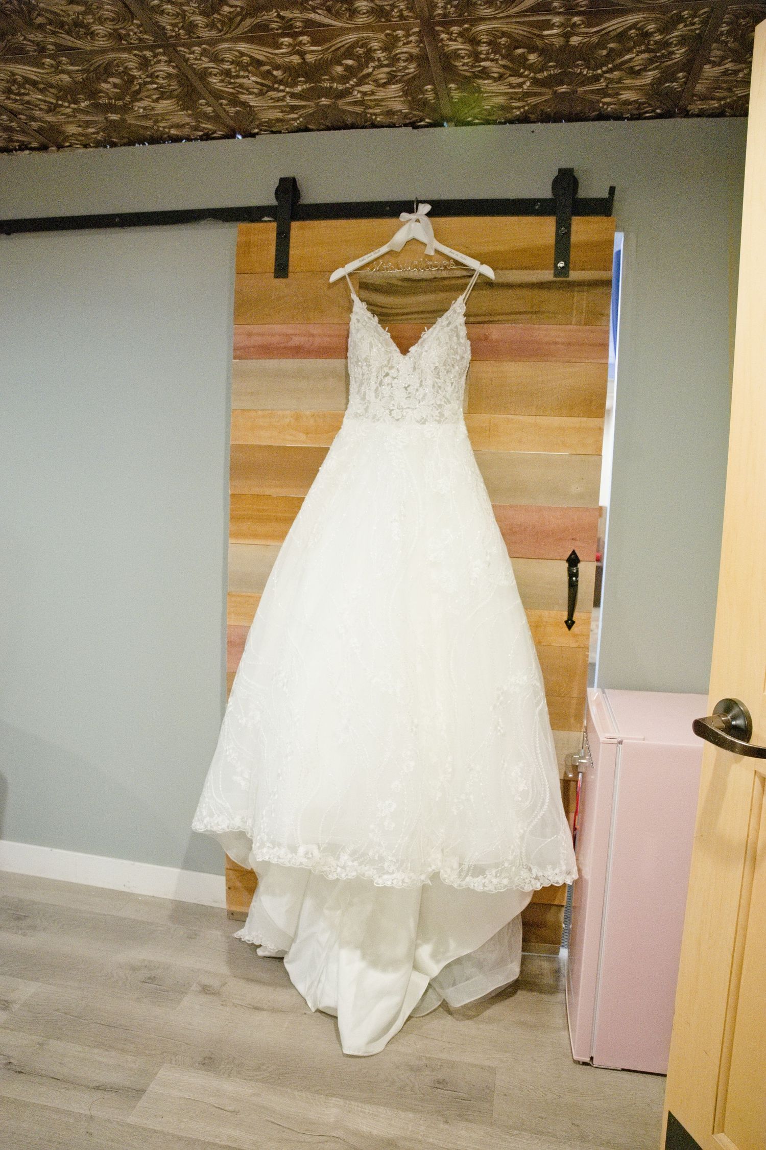 Beautiful white lace A-line wedding gown hanging on a sliding barn door in a bridal suite.