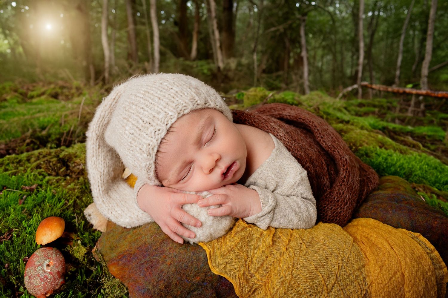 Sleeping baby in knit cap lies peacefully on mossy forest ground with autumn decor and sunlit trees in background. Princeton MN Milestone, M