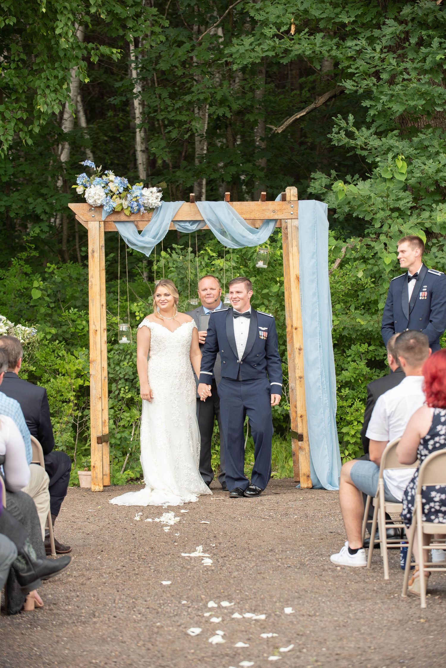 Wooden arch decorated with blue fabric and flowers set up for an outdoor forest wedding ceremony. Zimmerman MN Weddings